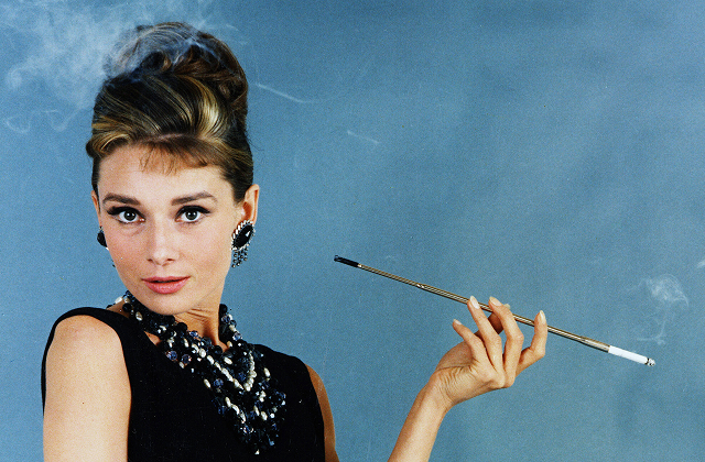 A vivid color photograph of Audrey Hepburn as Holly Golightly in the classic 1961 film 'Breakfast at Tiffany's,' wearing her iconic black gown and pearl necklace.