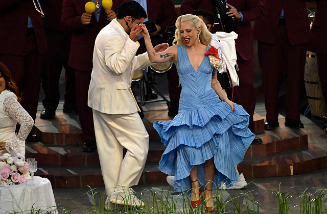 A high-energy moment from the Super Bowl halftime show, with Bad Bunny performing on stage as Lady Gaga dances in the foreground.