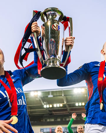 Players lift a trophy celebrating a women's football title win.